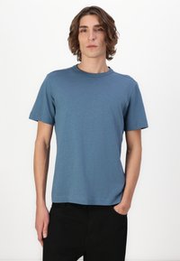 Tricou scurt cu mânecă în nuanță de albastru, confecționat dintr-un material moale, cu decolteu rotund. Are un logo mic pe piept și un croi lejer.