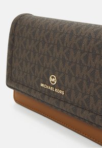 Braune und beige gemusterte Geldbörse mit MK-Logo, goldenen Hardware-Details und strukturiertem Äußeren. Der Verschlussklappen-Design verfügt über eine glatte Lederbasis.