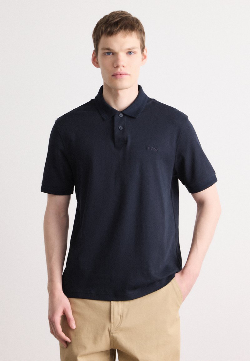 Cămașă polo bleumarin cu mâneci scurte, placket cu trei butoane și un logo subtil pe piept. Fabricată dintr-un material neted și respirabil.