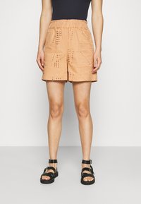 Shorts de couleur pêche avec une taille élastique, présentant des motifs texturés et des découpes, associés à des sandales noires à lanières.