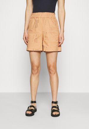 Shorts de couleur pêche avec une taille élastique, présentant des motifs texturés et des découpes, associés à des sandales noires à lanières.