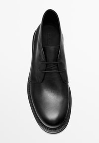 Chaussure à lacets en cuir noir avec une texture lisse, un bout arrondi et un design minimaliste. Les bords cousus ajoutent du détail à la silhouette classique.