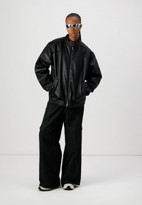 Veste bomber en cuir noir avec fermeture éclair à l'avant, ourlet côtelé et deux poches latérales. Associée à un pantalon cargo noir ample et des baskets blanches.
