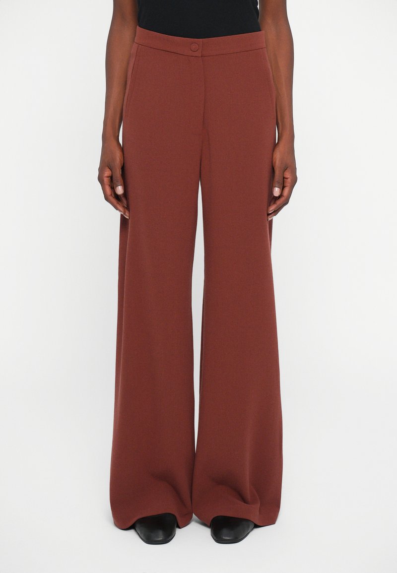 Pantalones de pierna ancha en un color óxido, hechos de una tela suave. Presentan un cierre de botón y una parte delantera plana con bolsillos laterales.