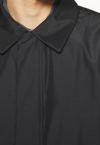 Black waterproof coat with a large collar, smooth texture, and visible stitching details, showcasing a simple, functional design.