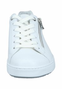 White leather sneakers feature a rounded toe, flat white laces, side zip closure, and a textured upper with a smooth rubber sole.