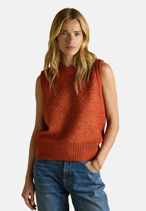 Ärmelloser Strickpullover in rostorange mit Diamantmuster und geripptem Saum, kombiniert mit blauen Jeans. Glatte Textur und lässiger Stil.