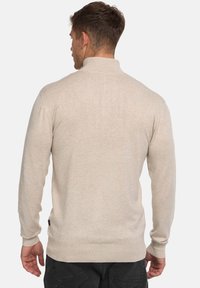 Maglione beige a maniche lunghe con collo alto, tessuto testurizzato, polsini e orlo a coste, con una piccola etichetta sul lato inferiore sinistro.