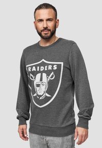 Grauer Rundhals-Sweatshirt mit einem großen weißen Raiders-Logo auf der Vorderseite. Lange Ärmel, gerippte Bündchen und Saum. Weicher Stoff.
