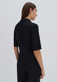 Chemise polo noire à manches courtes avec un col et une texture douce. Le design présente une coupe décontractée et des détails de couture subtils.