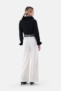 Black blouse with ruffled collar, paired with white wide-leg trousers featuring back pockets, worn with black high-heeled shoes.