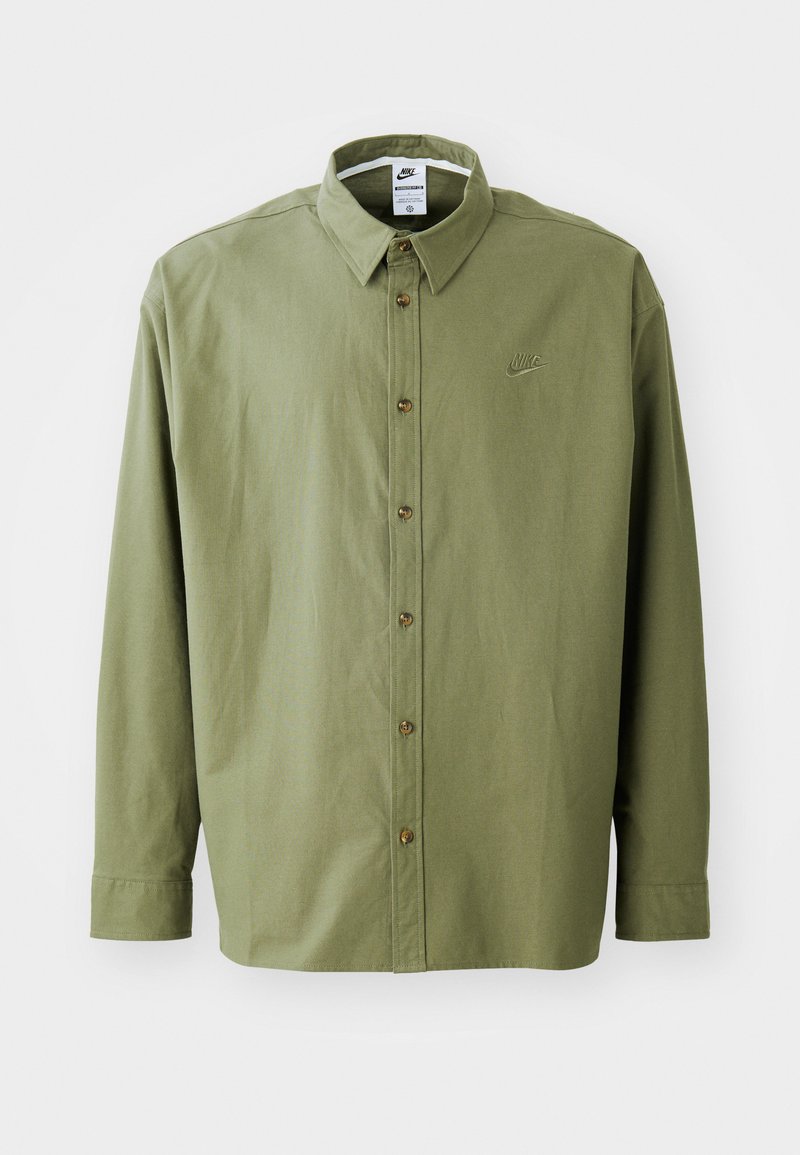 Camisa de algodón de color verde oliva, con cuello puntiagudo, mangas largas y un pequeño logo bordado en el pecho. Botones marrones.