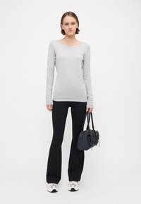 Top gri cu mânecă lungă, cu un model texturat, asortat cu pantaloni negri evazați și o geantă mică neagră. Pantofii sunt albi cu accente metalice.