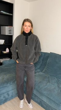 Γκρι φλις μπλουζάκι με μαύρο γιακά με φερμουάρ στη μέση, συνδυασμένο με γκρι παντελόνια ψηλόμεσα και λευκά αθλητικά παπούτσια με κόκκινες λεπτομέρειες.