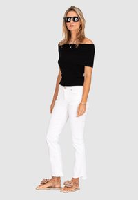 Black off-the-shoulder knit top, white flared jeans, beige sandals with floral accents, and oversized black sunglasses.
