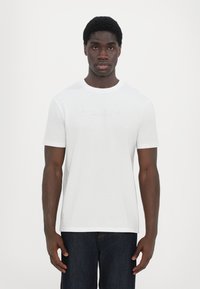 Hvit t-skjorte med korte ermer laget av bomull, med rund hals, og har en tonalt logo "ARMANI EXCHANGE MILANO/NEW YORK" på brystet.