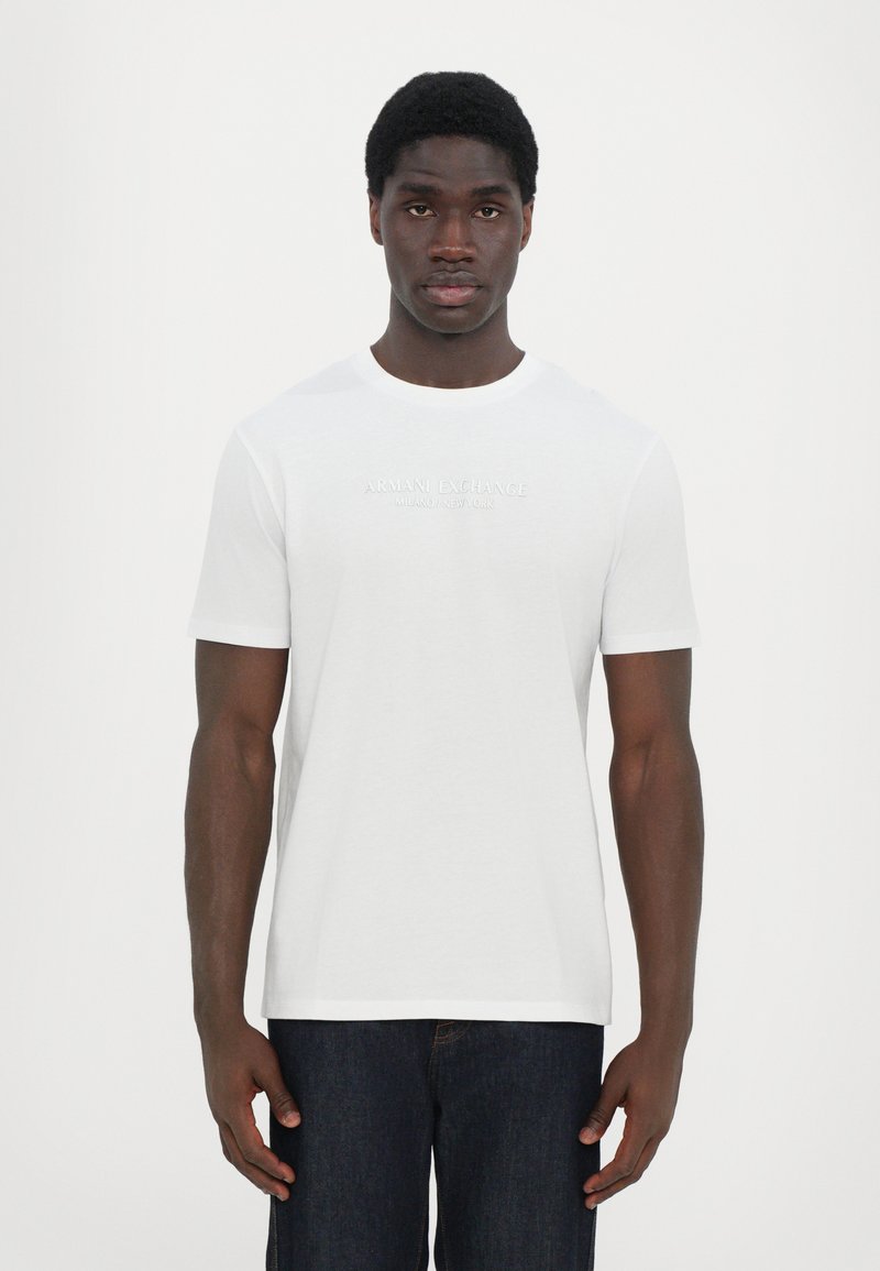 Hvit t-skjorte med korte ermer laget av bomull, med rund hals, og har en tonalt logo "ARMANI EXCHANGE MILANO/NEW YORK" på brystet.