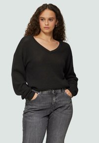 Zwarte gebreide trui met een V-hals en lange mouwen, gecombineerd met donkergrijze denim jeans. Casual pasvorm met een losse silhout.