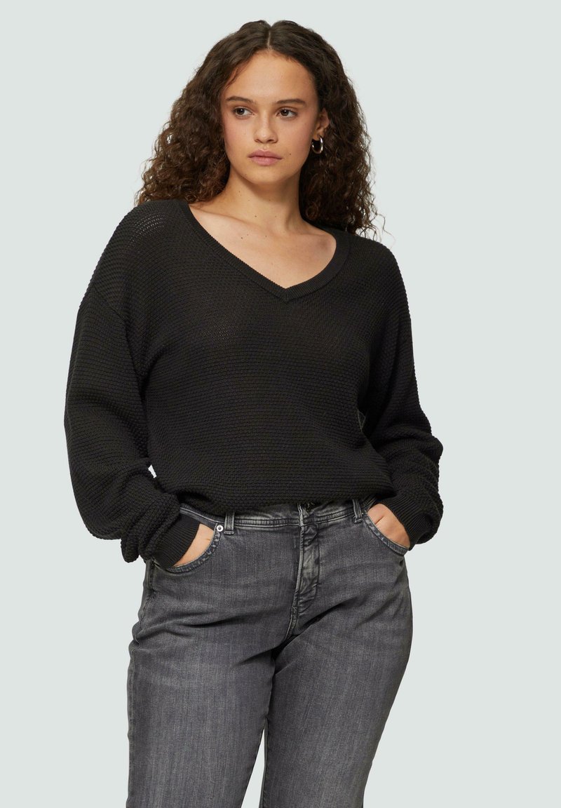 Zwarte gebreide trui met een V-hals en lange mouwen, gecombineerd met donkergrijze denim jeans. Casual pasvorm met een losse silhout.