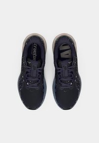 Zapatillas deportivas negras y moradas con parte superior de malla, suela texturizada y detalles moteados; presentan cordones y un interior acolchado.