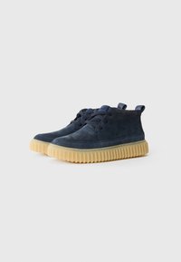 Navy blue suede shoes with a rounded toe and textured upper, featuring a gum rubber sole with vertical ridges and lace-up design.