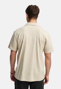 Korte mouw lichtbeige shirt met een gestructureerd, geribbeld patroon, met een omgeslagen kraag en een rechte zoom.