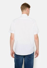 Camisa blanca de manga corta hecha de tela ligera, con un corte recto, cuello y dobladillo redondeado. Combinada con pantalones vaqueros denim azules.