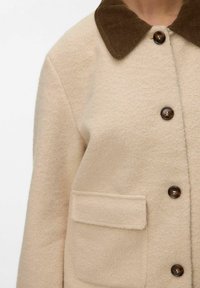 Manteau beige en mélange de laine avec un col en velours côtelé marron, doté de grands boutons marron et d'une poche avant. Tissu texturé et chaud.