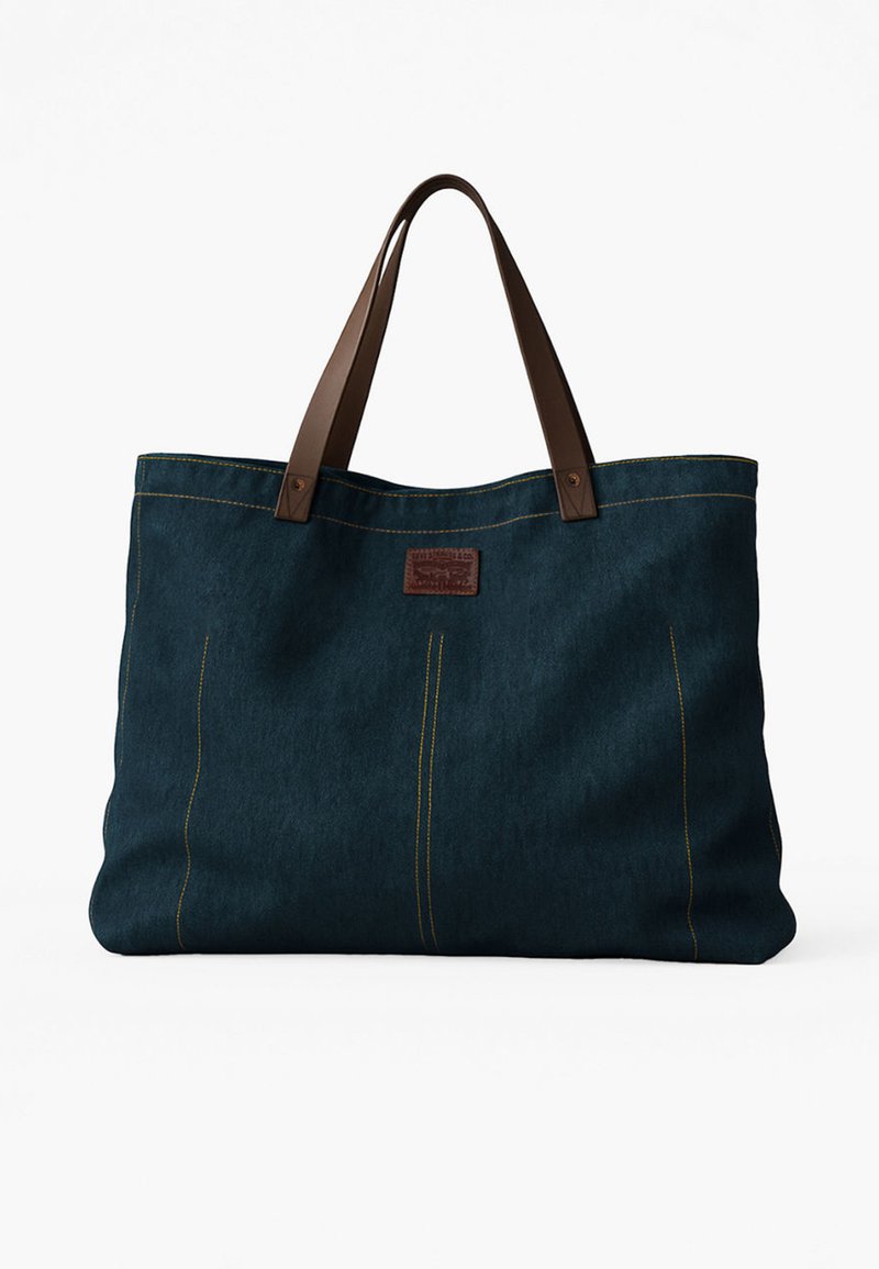 Borsa tote grande in tessuto blu scuro con manici in pelle marrone e cuciture gialle, con una piccola toppa rettangolare in pelle sul davanti.