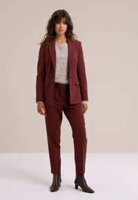 Burgundy skräddarsydd blazer och byxset med metallknappar; bärs över en ljusgrå strukturerad topp; avslutat med bruna stövlar i ankellängd.