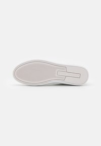 Semelle de chaussure en caoutchouc blanche avec un grip texturé et un branding subtil. Bout rond et bords lisses, conçus pour le confort et la stabilité.