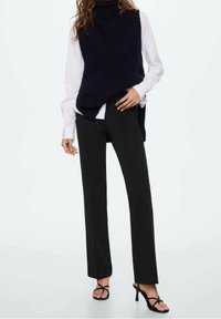 Navy knitted turtleneck sweater layered over a white collared shirt, paired with slim black trousers and black strappy heels.