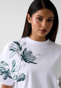 Wit katoenen T-shirt met groene bloemenborduursels en het "GUESS"-logo. Gestructureerde ronde hals en korte mouwen.