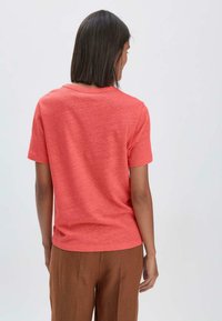 Koralli lyhythihainen t-paita pehmeästä, teksturoidusta kankaasta, pyöreällä kaula-aukolla ja rennolla istuvuudella, yhdistettynä ruskeisiin, pliseerattuihin housuihin.