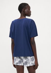 Navyblauw katoenen t-shirt met een relaxte pasvorm, wijde halslijn en korte mouwen, gecombineerd met witte shorts met een patroon.