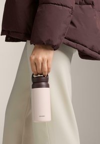 Stål vandflaske med en mat lys pink krop og en mørkebrun låg. Den har et robust håndtag til nem transport.