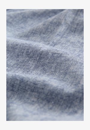 Tela de mezclilla azul claro con una textura suave, que muestra detalles de tejido fino y sutiles variaciones en el color con una apariencia ligeramente arrugada.