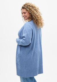Cardigan azzurro chiaro realizzato in materiale morbido, con orlo e polsini a coste, taschino e vestibilità comoda.