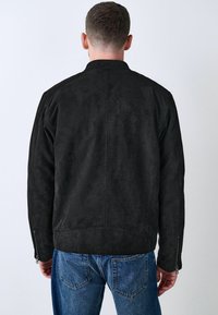 Sort ruskind jakke med en struktureret krave, lynlåse ved ærmerne og en glat tekstur. Har et rent design uden synlig branding.