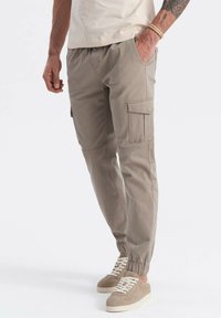 Beige cargobroek met elastische boorden, meerdere zakken en een ontspannen pasvorm. Gemaakt van lichtgewicht stof met versterkte stiksels.
