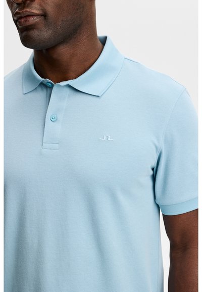 Uomo che indossa una polo a maniche corte azzurro chiaro con patta a due bottoni e piccolo logo bianco ricamato sul petto.