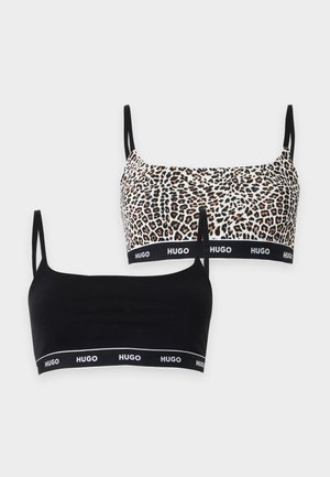 Femme portant un soutien-gorge imprimé léopard et une culotte assortie avec des bandes élastiques noires portant la mention « HUGO » sur un fond clair uni.