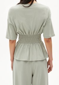 Světle zelený top s krátkými rukávy, pružným pasem a peplum designem. Hladká, měkká tkanina s volným střihem.