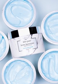Creamy body butter in a white jar with black marble accents. Bright blue smooth texture inside. Surrounded by similar white containers.
