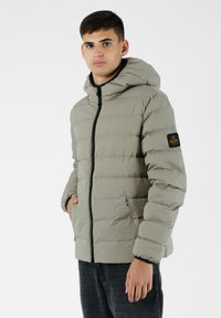 Giacca in piuma grigio chiaro con cappuccio, chiusura zippata e tasche laterali. Presenta una texture trapuntata e una toppa con logo sulla manica sinistra.