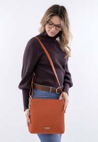 Orange leather crossbody bag with a textured finish, gold-tone hardware, and adjustable strap. Rectangular shape with a flat base.