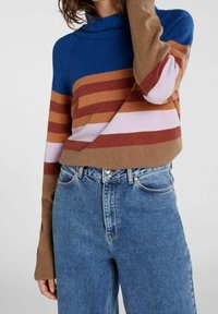 Sinivalkoraidallinen pooloneulepaita, jossa pitkät hihat, yhdistetty vaaleansinisiin korkeavyötäröisiin farkkuihin. Pehmeä neulosrakennelma.