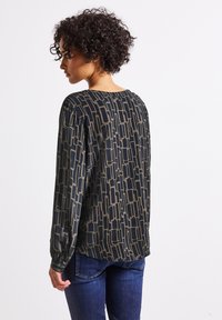 Chemise à manches longues de couleur vert foncé avec un motif géométrique beige ; tissu léger, coupe décontractée, encolure ronde et manches froncées.