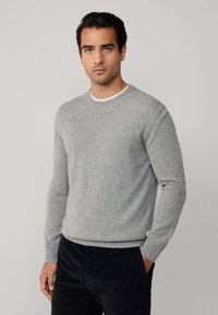 Jasnoszara sweter wykonany z miękkiego materiału, z okrągłym dekoltem, prążkowanymi mankietami i dołem. Nosi się go z ciemnymi spodniami o dopasowanym kroju i minimalistycznym designie.