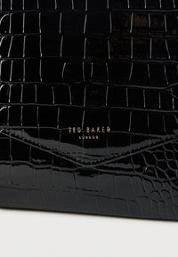 Fekete, krokodilmintás bőrtáska fényes kivitelben. Arany "Ted Baker London" logóval és hajtogatott kialakítással.
